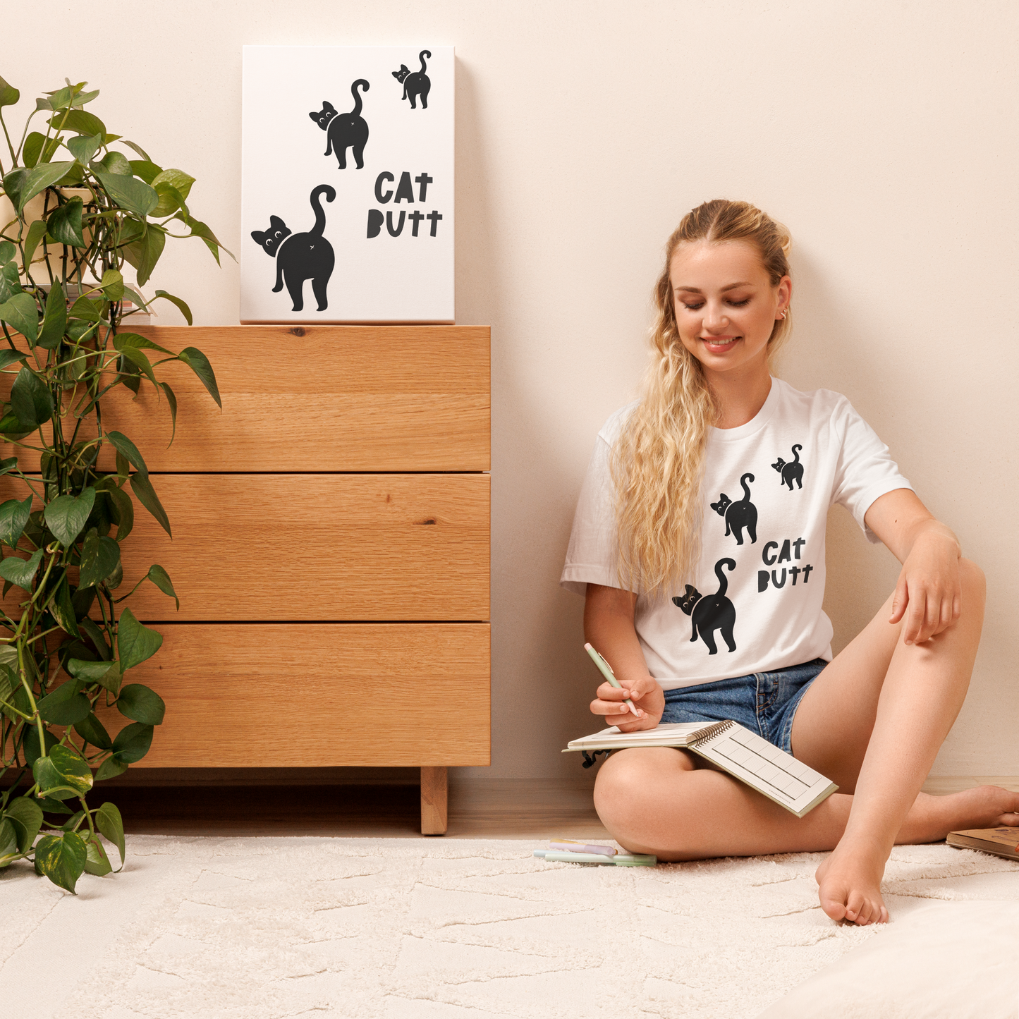 Woman sitting on the floor with a book, wearing a white t-shirt with black cat illustrations and text.