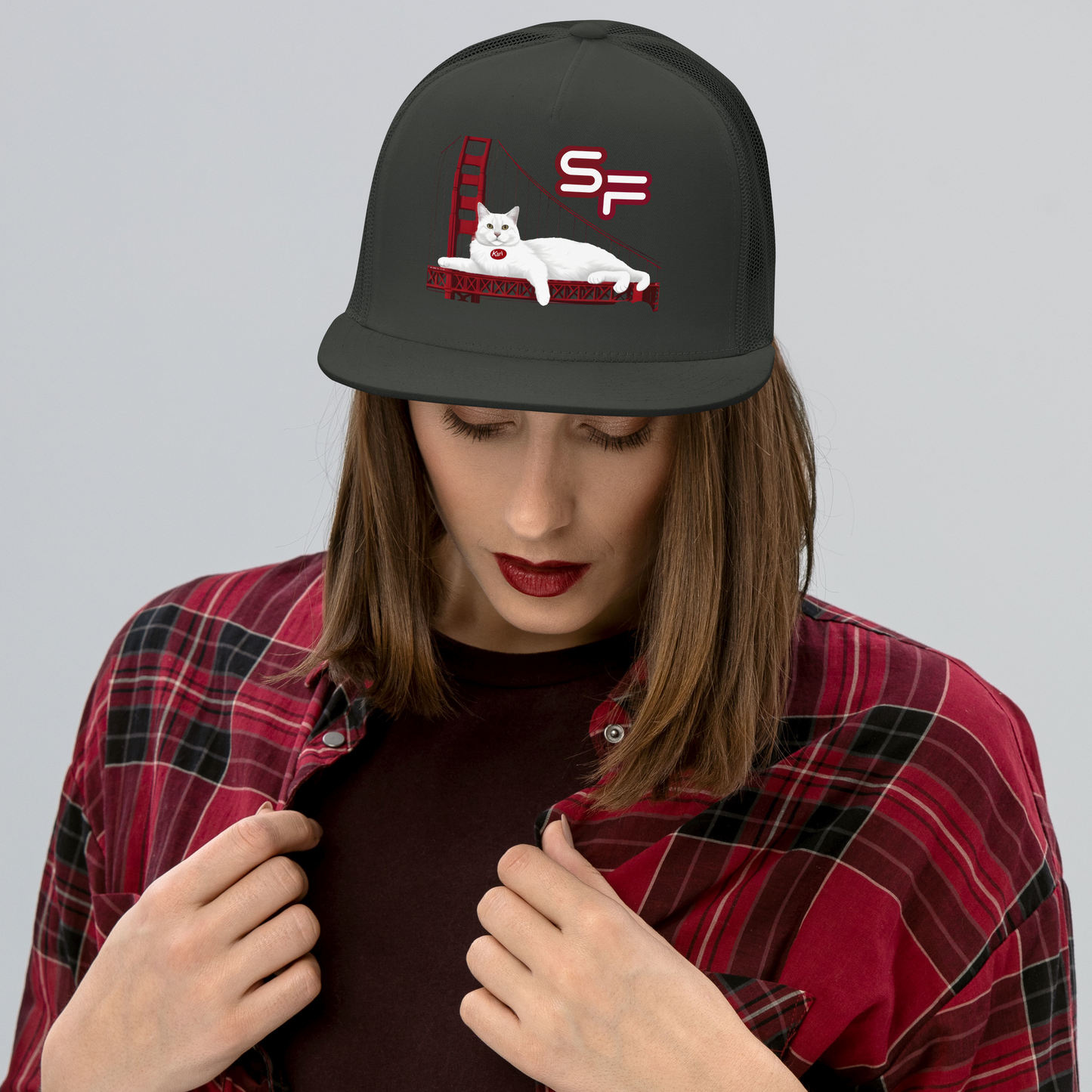 Person wearing a black cap with a cat design and plaid shirt on a gray background