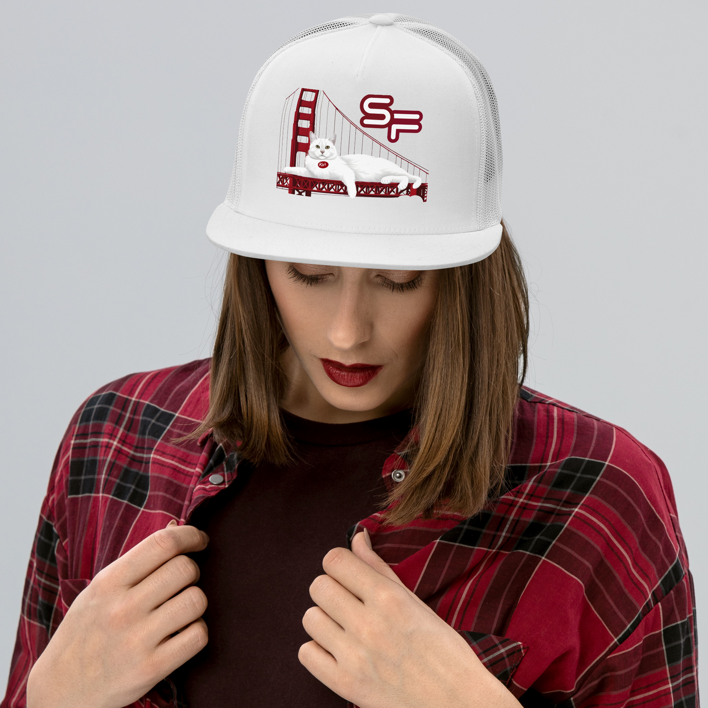 Person wearing a white cap with a design and red plaid shirt on a gray background