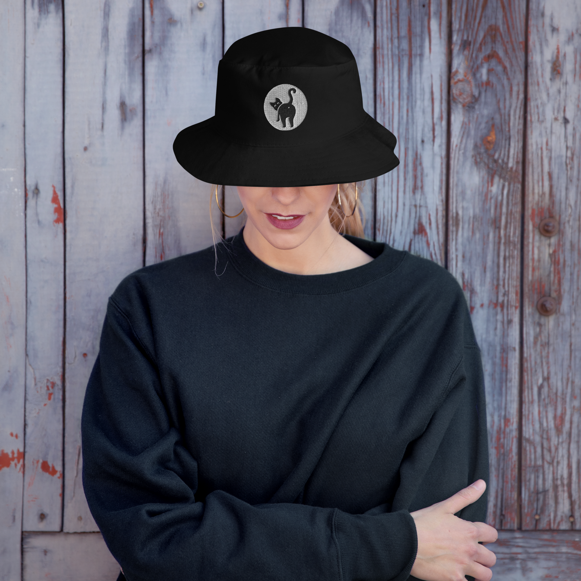 Person wearing a black bucket hat with a logo against a wooden background - black