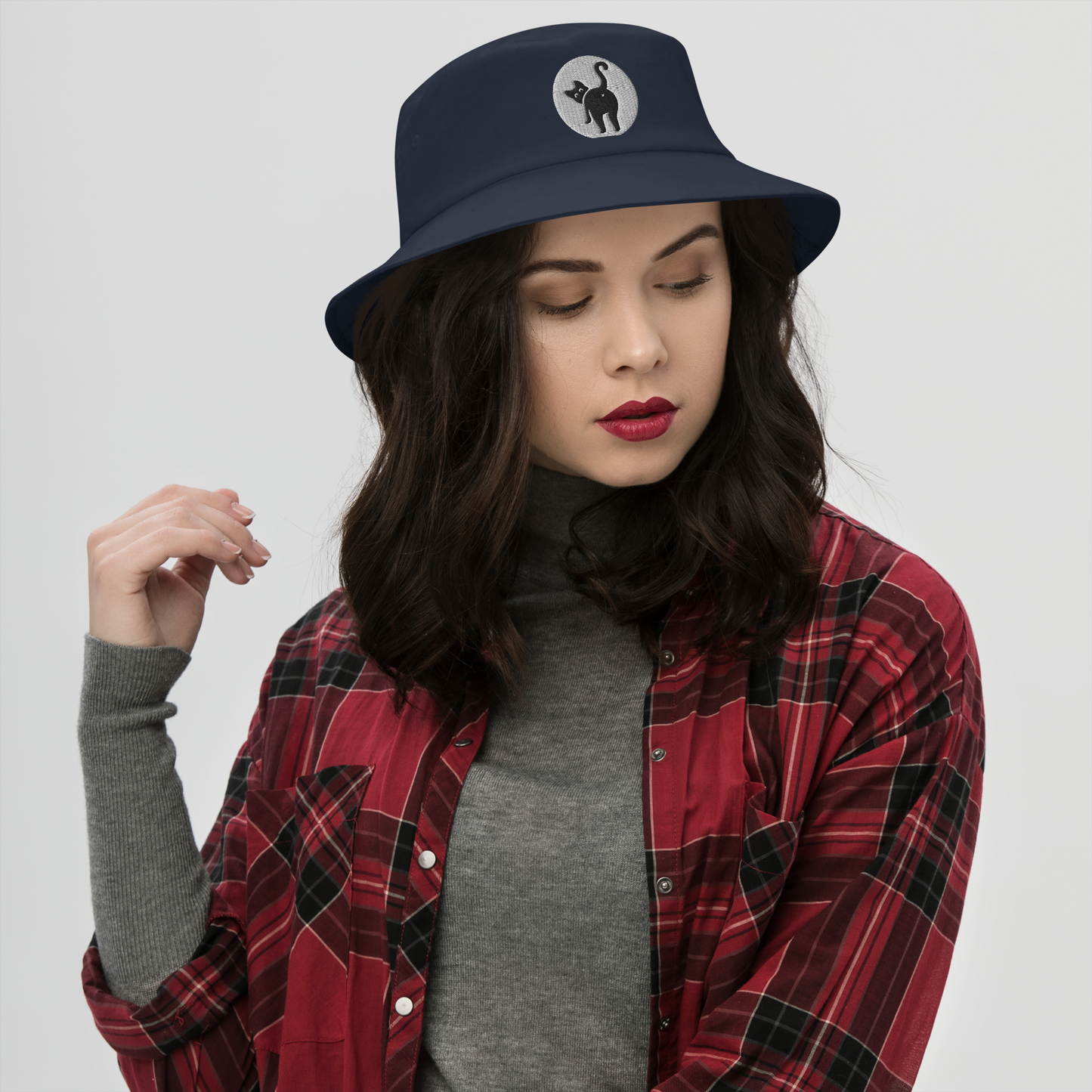 Woman wearing a navy bucket hat with a logo and a red plaid shirt on a white background - navy