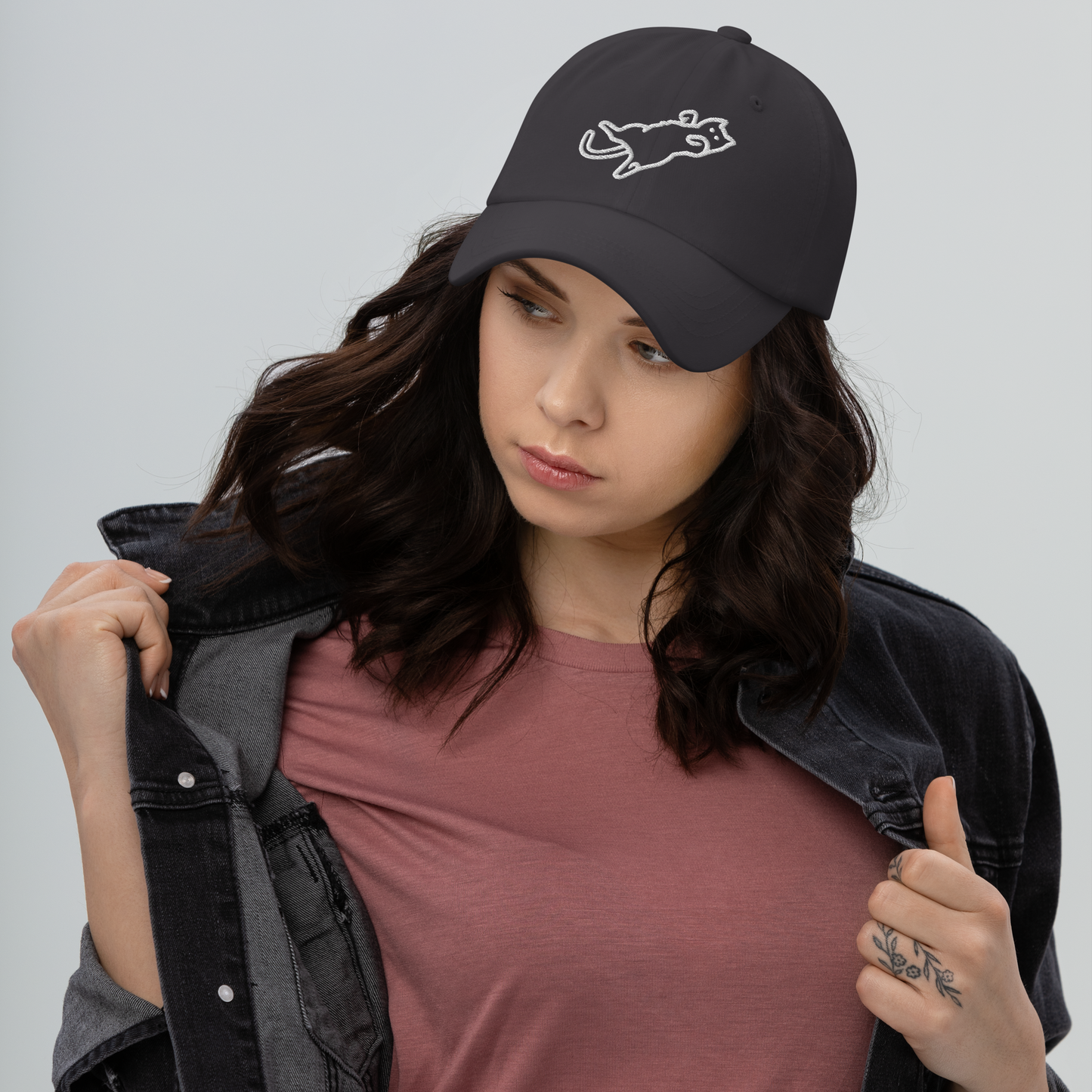 Woman wearing a black cap with a logo, holding a jacket, on a gray background - dark grey