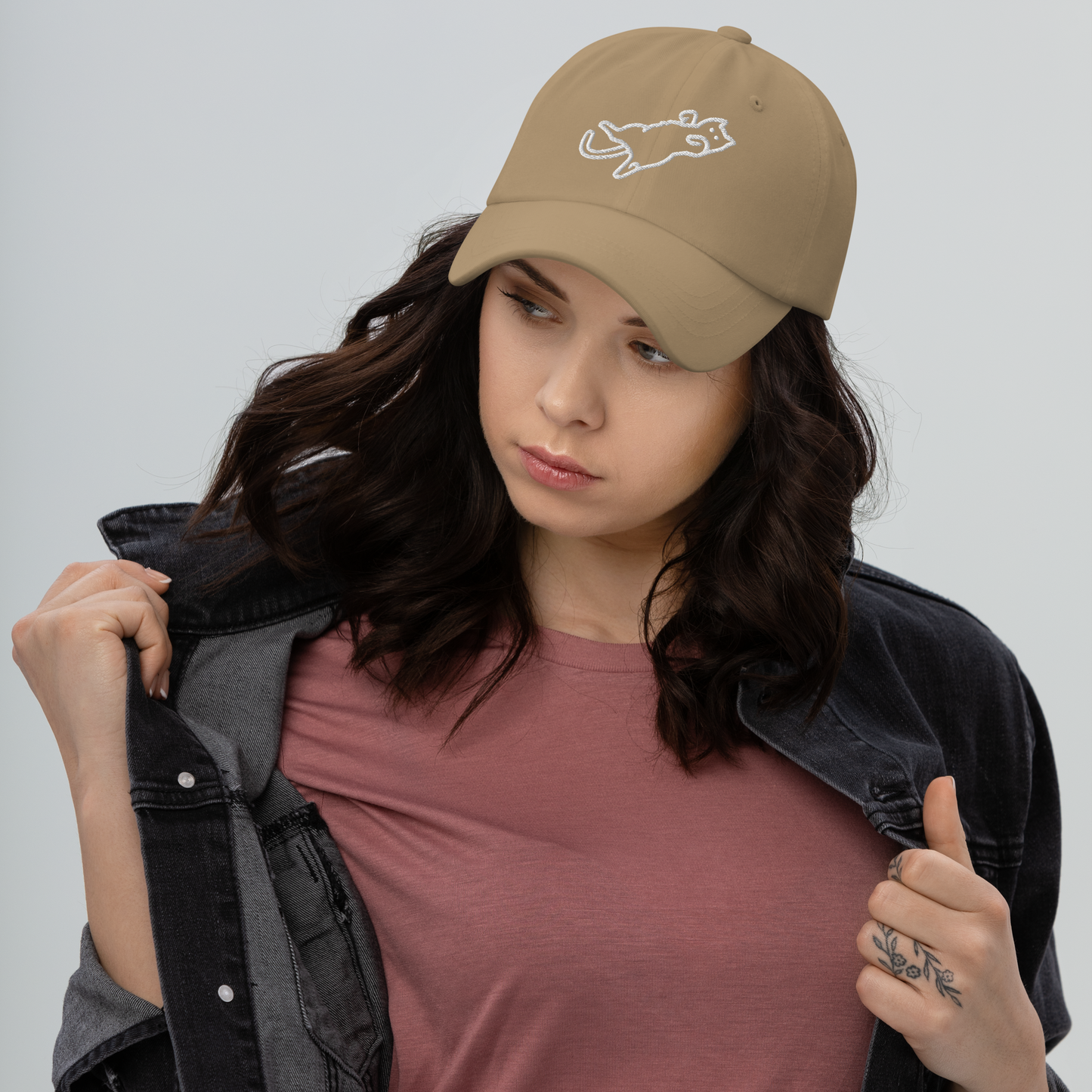 Woman wearing a brown cap with a logo, holding a black jacket against a gray background - khaki