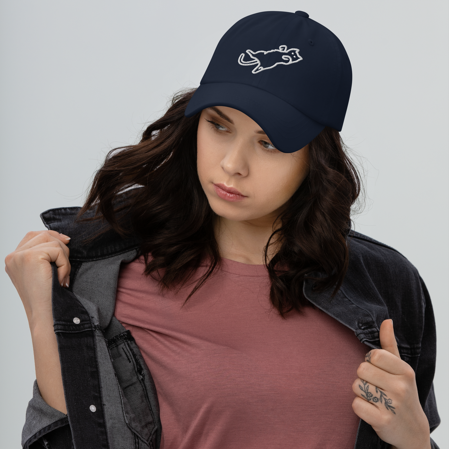 Woman wearing a navy blue cap with a logo, holding a black jacket against a gray background - navy