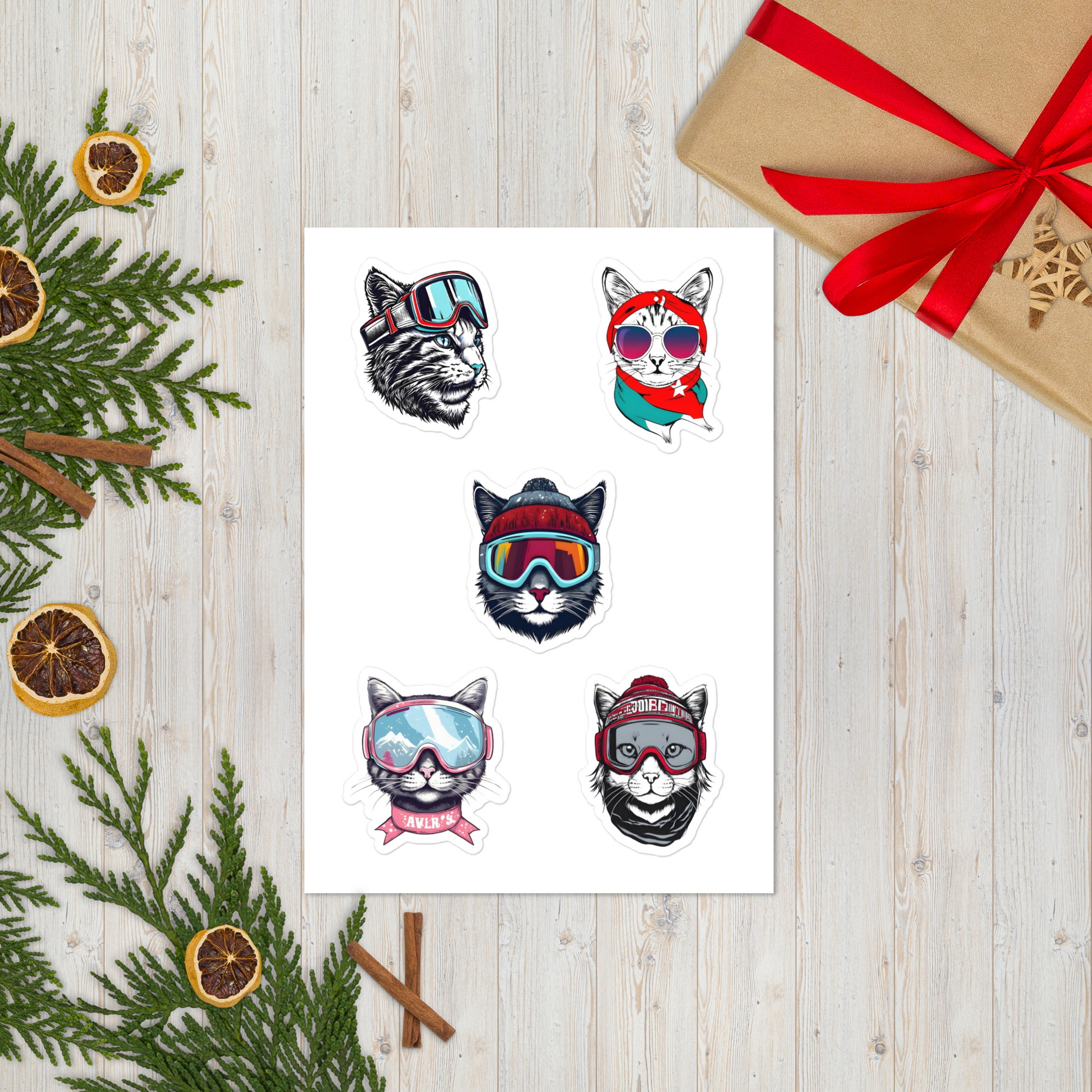 Sheet of temporary tattoos with cat designs wearing colorful goggles on a wooden surface with Christmas decorations.