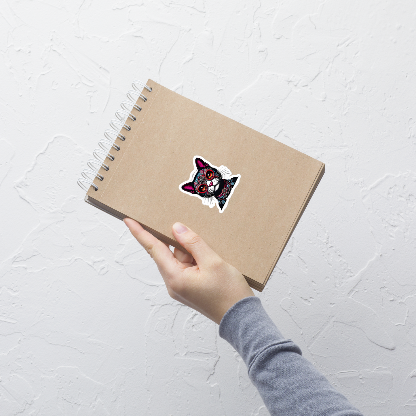 Hand holding a brown notebook with a sticker on a light gray background - 3"x3"