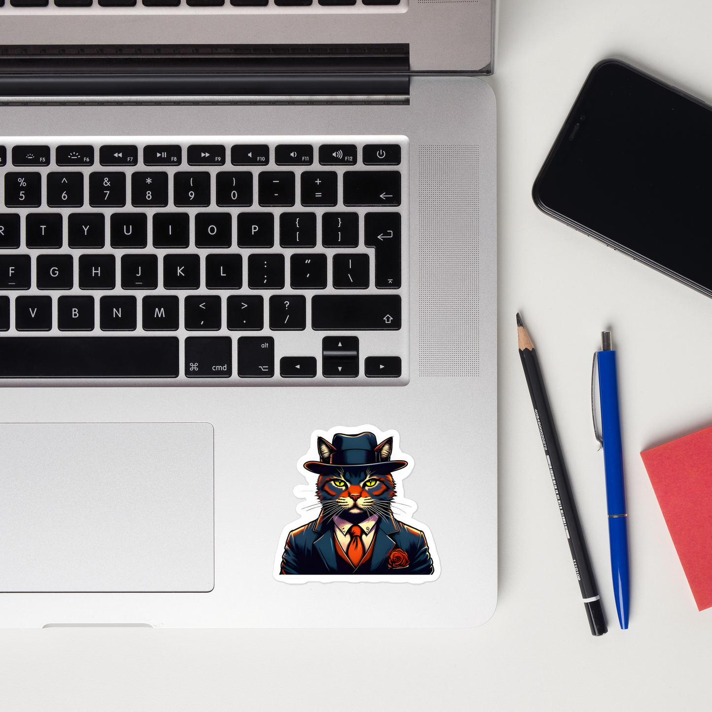 Laptop with a cat in a suit sticker, phone, pencil, pen, and notebook on a white surface - 3"x3"