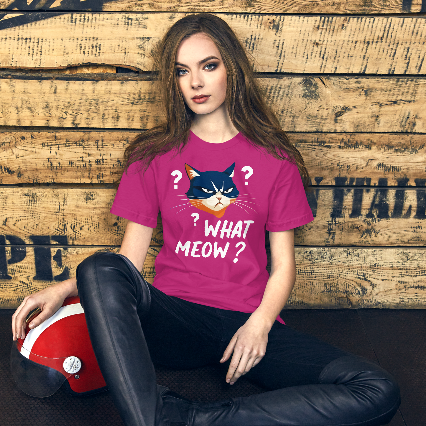 Woman wearing a pink t-shirt with a cat graphic and text, sitting against a wooden wall. - berry