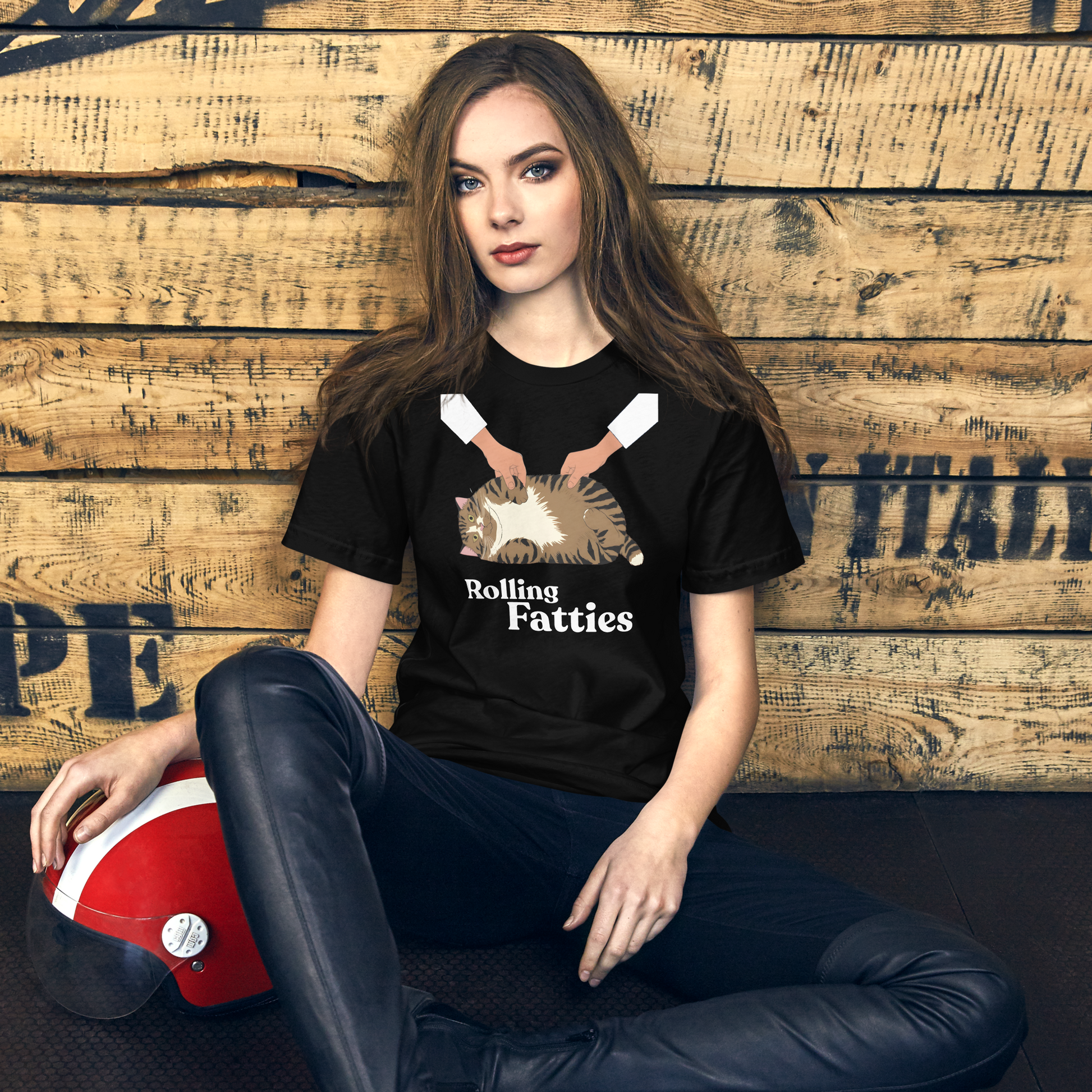 Woman wearing a black t-shirt with 'Rolling Fatties' graphic design, sitting against a wooden wall. - black