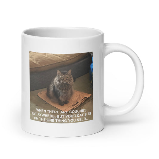A white glossy mug with a cat meme about sitting on the one thing you need. The handle is to the right - 20 oz